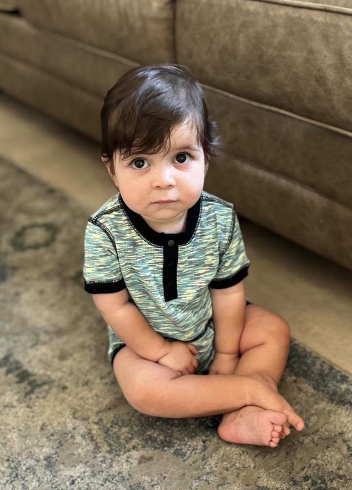 Gabriel Zev sitting on a rug in a patterned romper