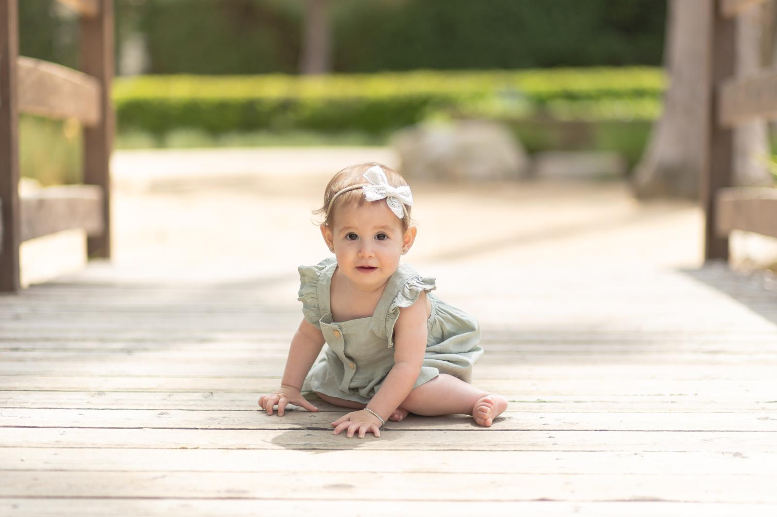 Leah Adel crawling on a wooden bridge in a green romper