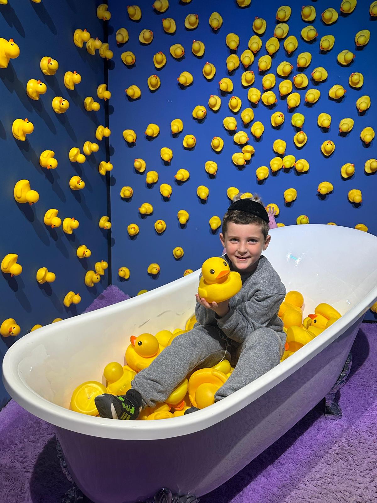 Yonatan Tsvi sitting in a bathtub full of rubber ducks